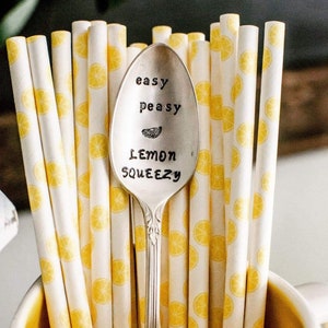 Puede incluir: Una cuchara de plata con las palabras "easy peasy lemon squeezy" grabadas en ella. La cuchara est&aacute; rodeada de pajitas rayadas de color amarillo y blanco con un patr&oacute;n de lim&oacute;n.
