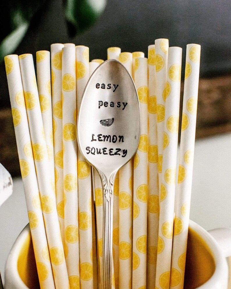 Puede incluir: Una cuchara de plata con las palabras "easy peasy lemon squeezy" grabadas en ella. La cuchara est&aacute; rodeada de pajitas rayadas de color amarillo y blanco con un patr&oacute;n de lim&oacute;n.