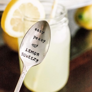 Puede incluir: Una cuchara de plata con las palabras "easy peasy lemon squeezy" grabadas en ella. La cuchara est&aacute; delante de un vaso de limonada con una rodaja de lim&oacute;n.