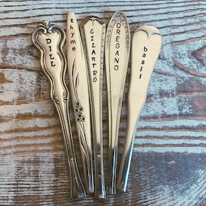 May include: Five vintage silverware spoons with the words "Dill", "Thyme", "Cilantro", "Oregano", and "Basil" engraved on them.