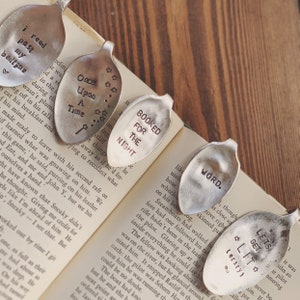 May include: A set of ten silver spoons with engraved text, including "I read past my bedtime", "Once Upon A Time", "Booked for the Night", "Word", and "Let's Get Literary". The spoons are arranged on an open book.