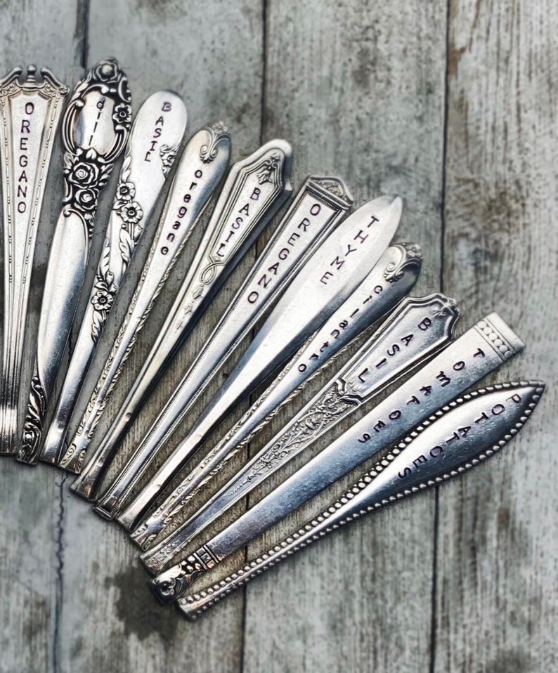 May include: A collection of vintage silverware spoons with various herbs and spices names engraved on them, including oregano, basil, thyme, and rosemary.