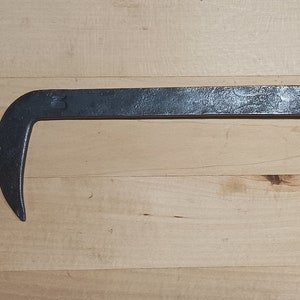 May include: A twisted metal hook with a sharp point at the end. The hook is made of dark metal and has a rustic appearance.