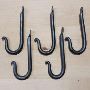 May include: Six black metal hooks with a decorative curl at the end. The hooks are all the same size and shape.