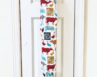 May include: A white fabric bag dispenser with a black handle. The bag is printed with farm animals, including cows, chickens, pigs, and ducks. The text "Farm Fresh Farm" is repeated on the bag.