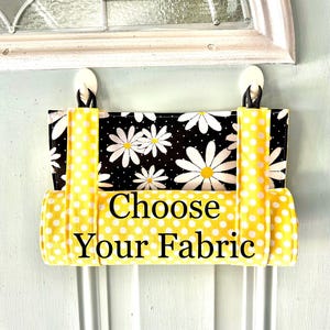 May include: A yellow and white polka dot fabric door hanger with the text "Choose Your Fabric" in black. The hanger has a black and white daisy print on the back.