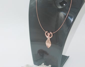 May include: A copper-coloured pendant necklace displayed on a black mannequin. The pendant features a stylized female figure design. Two crystals, one pink and one white, are at the base of the mannequin. The necklace has a delicate chain.