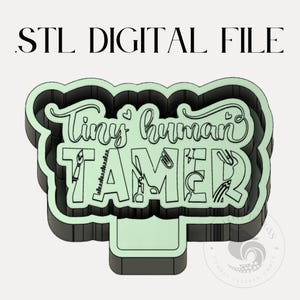 以下が含まれることがあります： 緑色の背景と黒い輪郭を持つ「Tiny Human Tamer」のサインの3Dプリント可能なSTLファイルです。サインは、風変わりなフォントを使用しており、ツールや学用品の小さなイラストが含まれています。