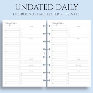 May include: A white undated daily planner with a gray and white binding. The planner has two pages with sections for "Today's Date", "Top 3", "Notes", "Water", "Exercise", and "Meals".