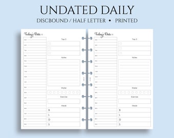 May include: A white undated daily planner with a gray and white binding. The planner has two pages with sections for "Today's Date", "Top 3", "Notes", "Water", "Exercise", and "Meals".