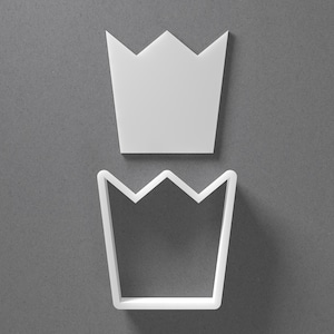 May include: Two white crown-shaped objects. One is a solid crown, and the other is a crown-shaped outline. The objects are placed on a gray background. The crown shapes are likely cookie cutters or craft supplies.