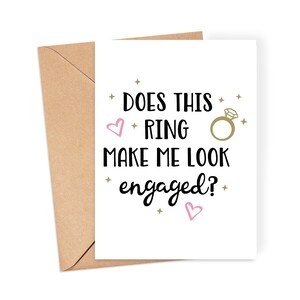 May include: A white card with black text that reads "Does this ring make me look engaged?" with a gold ring and pink hearts.