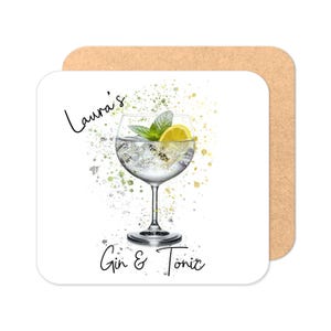 May include: A square coaster with a watercolor illustration of a gin and tonic cocktail. The drink is in a stemmed glass with ice, a lemon slice, and mint leaves. The text "Laura's Gin & Tonic" is written on the coaster.