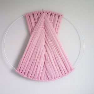 May include: A pink yarn wall hanging with a woven design, created on a circular metal hoop.