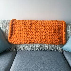 May include: A bright orange chunky knit throw blanket on a gray couch with two blue throw pillows.
