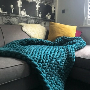 May include: A teal chunky knit throw blanket draped over a gray couch with white and yellow throw pillows.