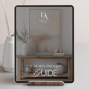 Può includere: Un tablet digitale che mostra una guida al processo di progettazione per Denise Alva Interiors. La guida è su un tavolo di legno con un vaso di rami e un dipinto sullo sfondo.