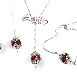 Può includere: Un set di gioielli a catena d'argento con ornamenti di perline rosse e bianche. Il set comprende una collana, un braccialetto e un paio di orecchini.