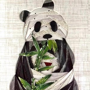 May include: A black and white panda bear made of fabric scraps is holding a bunch of green bamboo stalks. The panda is wrapped in white fabric, resembling bandages.