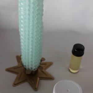 May include: A teal honeycomb candle on a gold star-shaped candle holder, a small clear bottle with a black lid containing oil, and a small white jar with a brown substance inside.