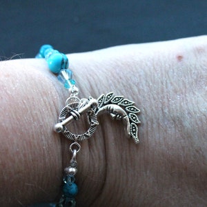 May include: A turquoise and silver bracelet with a decorative clasp featuring a crescent moon and leaves. The bracelet is made with turquoise beads and silver beads.