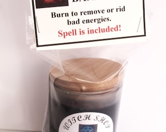 May include: A black crystal herbal candle in a glass jar with a wooden lid, labeled "BANISHING." The label includes text: "Burn to remove or rid bad energies. Spell is included!" and a "Witch Shop" logo.