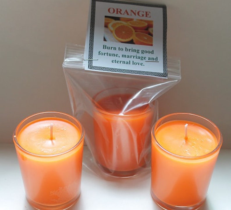 May include: Three orange-colored votive candles in clear glass holders. One candle is in a plastic bag with a label that reads "ORANGE" and "Burn to bring good fortune, marriage and eternal love."