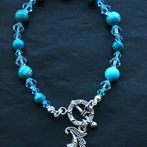May include: A turquoise and silver bracelet with a crescent moon charm. The bracelet is made with turquoise beads and clear crystal beads.