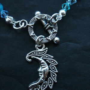 May include: A silver necklace with a crescent moon charm and a toggle clasp. The necklace is made of silver beads and turquoise stones.