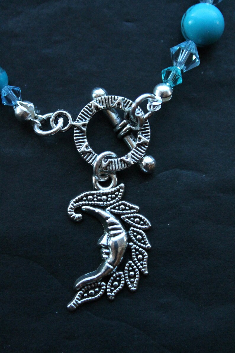 May include: A silver necklace with a crescent moon charm and a toggle clasp. The necklace is made of silver beads and turquoise stones.