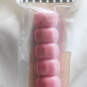 May include: A pink wishing candle in a clear plastic bag. The candle is shaped like a stack of small circles. The label on the bag reads "Wishing Candle Pink Attract Friendship, Love and Romance."