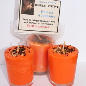 May include: Three orange votive candles in clear glass holders. The candles have a speckled topping and a white wick. A card reads "POWER WITHIN HERBAL VOTIVE Harvest Abundance. Burn to bring abundance, love and answers to your wishes. Spell is included."