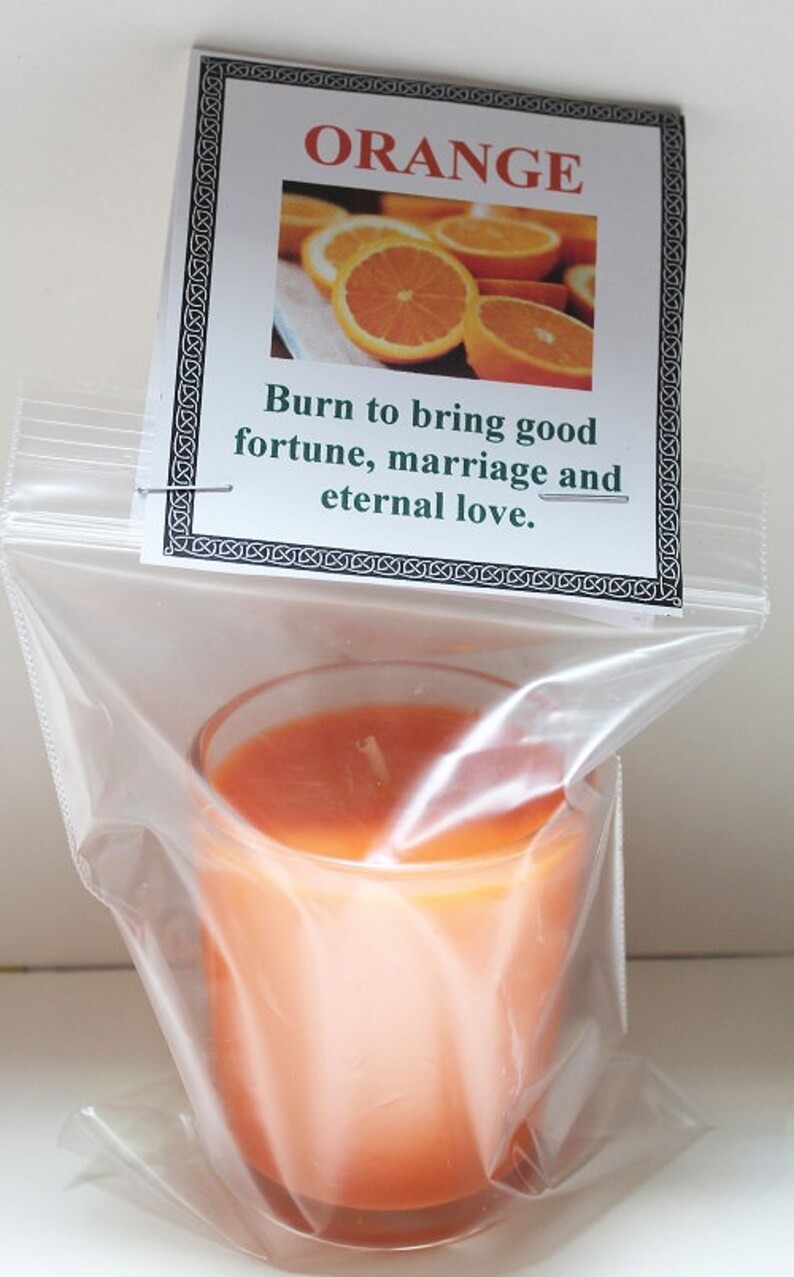 May include: Orange-scented candle in a clear glass, packaged in a plastic bag. The candle is a vibrant orange color. A tag above the candle reads "ORANGE" with an image of orange slices and the text "Burn to bring good fortune, marriage and eternal love."