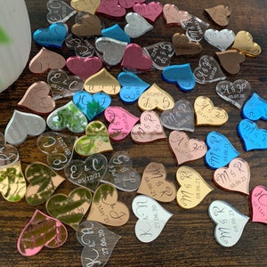 May include: Assortment of heart-shaped confetti with various colors and mirrored surfaces. Each heart has a personalized inscription with names and dates.