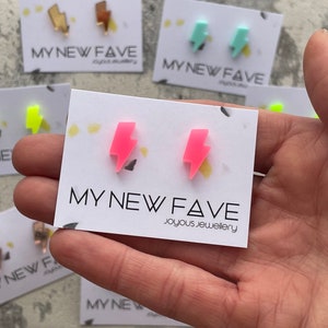 May include: A pair of pink lightning bolt stud earrings on a white card with the text "MY NEW FAVE joyous jewellery".