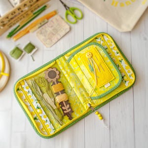 May include: A fabric sewing organizer case featuring a bright yellow lemon pattern with green trim. The interior includes a zippered pocket, a felt needle book with a yellow button, and a brown wooden thread winder holding green and yellow embroidery floss.