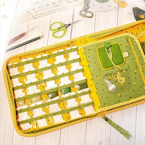 May include: Open yellow and green fabric craft organizer with thread spools, scissors, and other sewing supplies. The organizer has a zippered closure and a gingham pattern trim. The interior features clear pockets and compartments for storage.