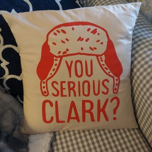 May include: A white pillow with a red and white illustration of a winter hat and the text "You serious Clark?" printed on it.