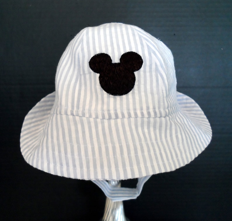 Op de afbeelding: Een blauwe en witte gestreepte zonnehoed met een zwart Mickey Mouse silhouet aan de voorkant.