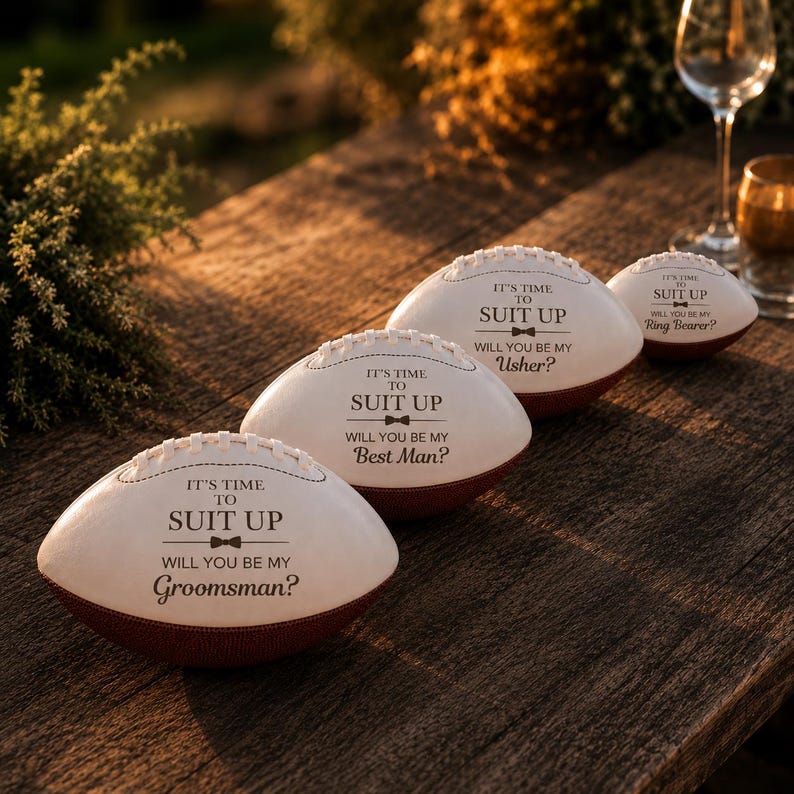 Puede incluir: Tres balones de f&uacute;tbol americano blancos y marrones con texto negro que dice IT'S TIME TO SUIT UP seguido de WILL YOU BE MY GROOMSMAN, WILL YOU BE MY BEST MAN o WILL YOU BE MY USHER, adem&aacute;s de un bal&oacute;n m&aacute;s peque&ntilde;o con WILL YOU BE MY RING BEARER.