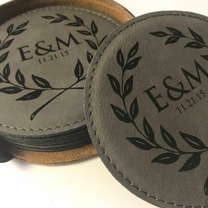 Puede incluir: Conjunto de posavasos de cuero gris con un diseño negro de una corona y las iniciales "E&M" y la fecha "11.21.15".