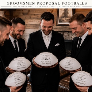 Puede incluir: Balones de f&uacute;tbol americano blancos con texto negro que dice IT'S TIME TO SUIT UP WILL YOU BE MY GROOMSMAN? o WILL YOU BE MY BEST MAN? Los balones tienen un peque&ntilde;o gr&aacute;fico de pajarita negra y son sostenidos por personas con trajes negros.