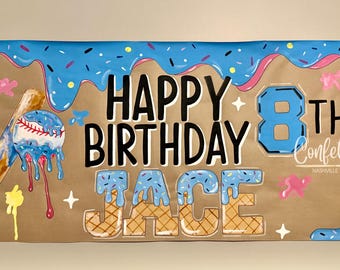May include: A brown banner with blue, pink, and yellow accents. The words "HAPPY BIRTHDAY JACE 8TH Confetti Nashville" are written in black and blue. A baseball bat and ball are depicted with blue icing.