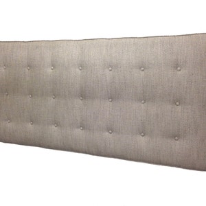 May include: A large, rectangular headboard upholstered in a light grey fabric with a subtle textured pattern. The headboard is tufted with evenly spaced buttons.