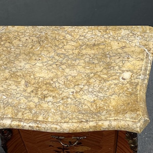 May include: A detailed overhead shot of a small, antique wooden cabinet with a marble top. The marble is a light beige color with intricate brown and gray veining. The cabinet has a decorative drawer pull and ornate carvings.