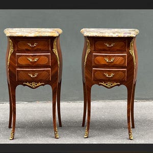 Può includere: Due comodini antichi abbinati. Ognuno ha un piano in marmo, tre cassetti e dettagli dorati. Il legno è un marrone intenso con un'impiallacciatura a motivi. I comodini hanno gambe curve e ferramenta decorativa.