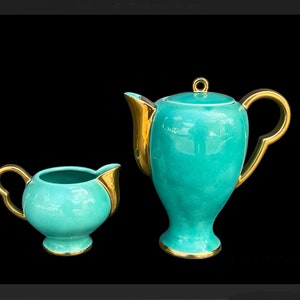 Könnte beinhalten: Ein Teekannen- und Milchkännchen-Set in blaugrüner Farbe mit goldenen Akzenten. Die Teekanne hat einen Deckel und einen geschwungenen Griff. Das Milchkännchen hat einen herzförmigen Griff.