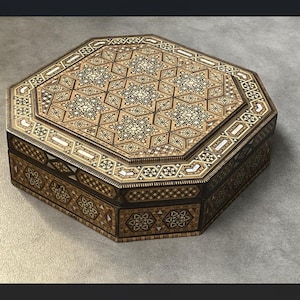Peut inclure: Une boîte octogonale en bois avec des motifs incrustés complexes. Le couvercle et les côtés présentent des motifs géométriques dans des tons de marron, beige et blanc. La boîte semble être faite à la main, mettant en valeur un savoir-faire détaillé et une esthétique décorative.