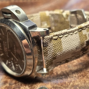May include: A silver wristwatch with a black face and a camouflage patterned fabric watch band.