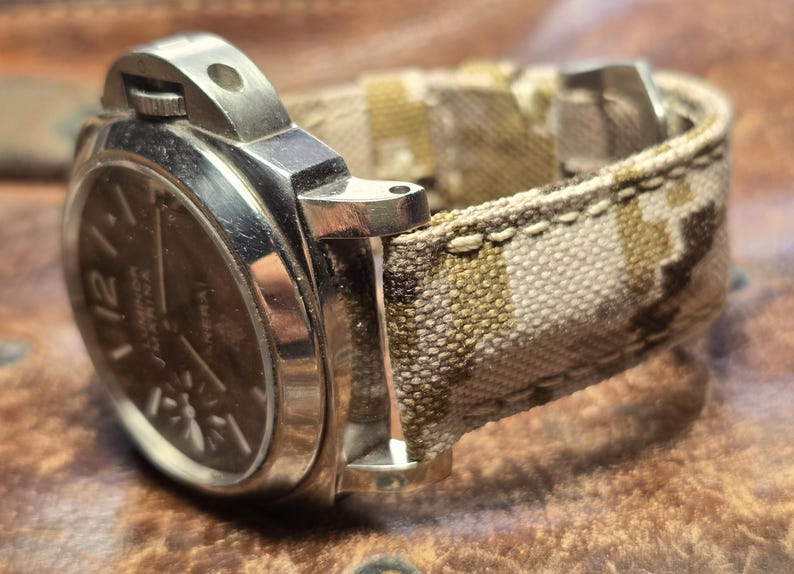 May include: A silver wristwatch with a black face and a camouflage patterned fabric watch band.